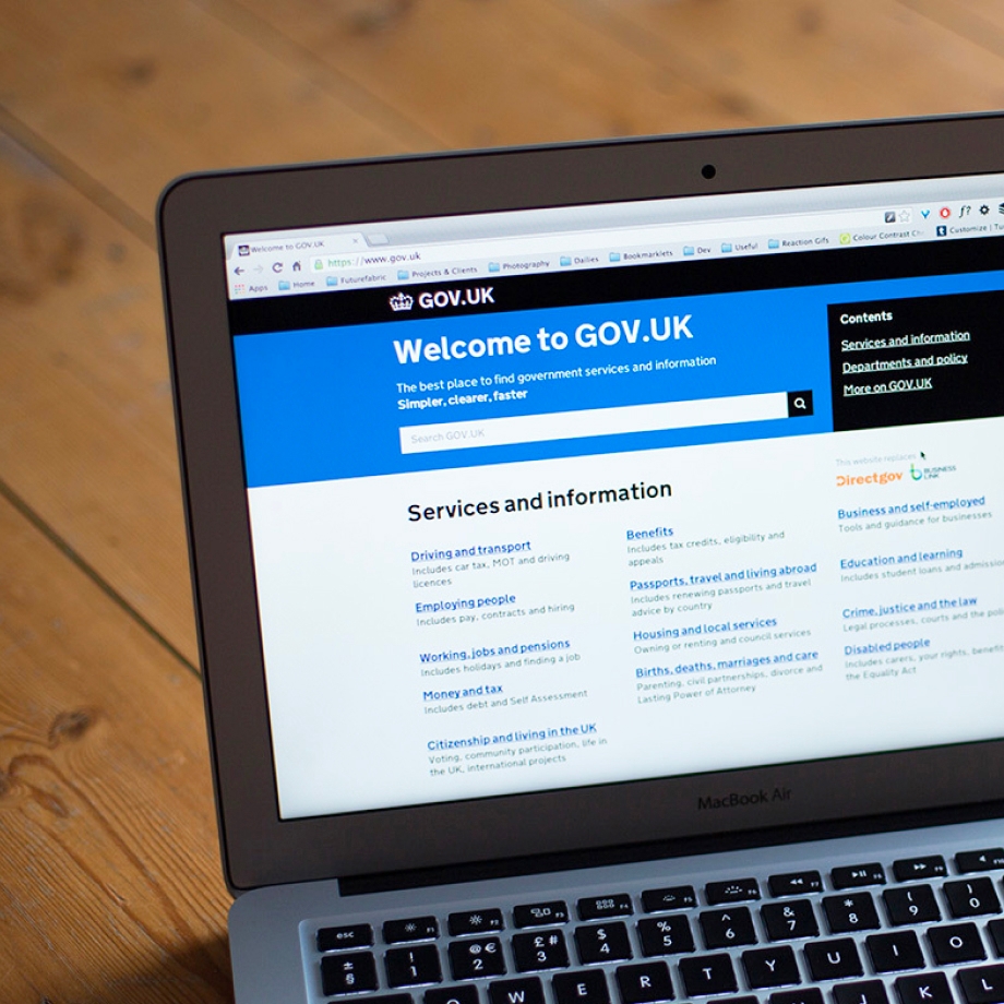 A photograph of a MacBook Air laptop showing the GOV.UK homepage on its screen.
